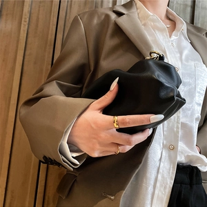 Minimalist black cloud-style leather clutch bag held by a model wearing rings