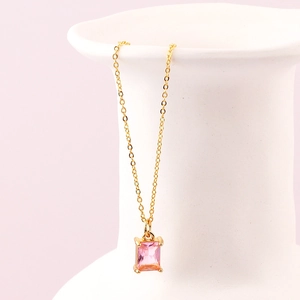 Dettaglio pendente in zircone rosa rettangolare con catena dorata su ceramica bianca