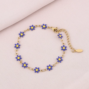 Detailed view of gold daisy chain bracelet with blue petals on a soft purple fabric