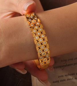 Detailed view of a gold openwork bangle with sparkling zircon clover patterns on wrist