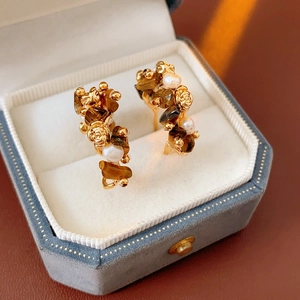 Close-up of golden flower C-shaped earrings with tiger eye stone and pearls in a box