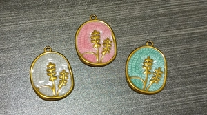 Detail of oval gold-plated stainless steel flower pendants with colorful enamel inlay