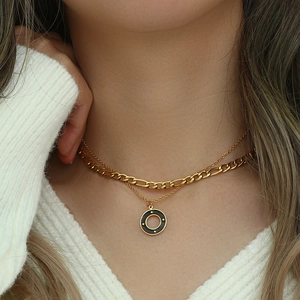 Detail of layered gold Figaro necklace with a black enamel circle pendant on a model