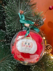 Nahaufnahme einer festlichen Weihnachtskugel mit roter Plüschpuppe und grünem Band-Detail