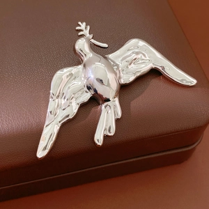 Macro detail of silver bird brooch with olive branch on brown leather box