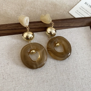 Detail of irregular acrylic earrings with gold metal accents on textured fabric