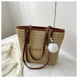 Detail of beige straw tote bag with brown leather handles and decorative white pompom