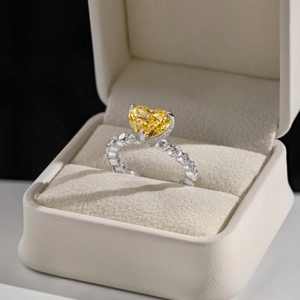 Macro shot of silver ring with yellow heart gemstone and side diamonds in a beige box