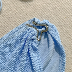 Close-up of light blue textured bikini fabric with a silver metallic buckle fastener