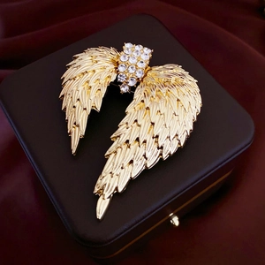 Détail de la broche ailes dorées ornée de strass posée sur un écrin en cuir