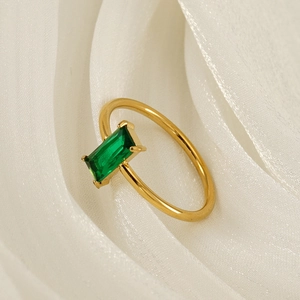 Golden titanium steel ring with emerald rectangular gemstone on white silk fabric