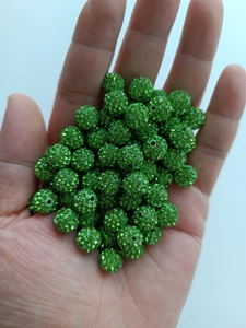 Close-up of 10mm sparkling green rhinestone clay disco beads held in hand for scale