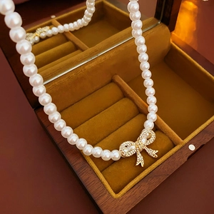 Gros plan d'un collier de perles avec pendentif noeud en diamant dans un écrin élégant