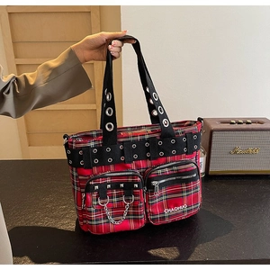 Detail of red plaid tote bag with metal grommets, chains and zip pockets in punk style