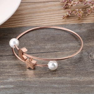 Rose gold twisted wire bangle with white pearls and star moon charms on wood background