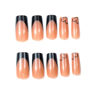 Detail of nude pink press-on nails with black French tips and heart patterns