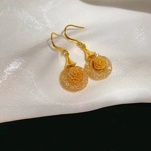 Close-up of golden mesh floral earrings with a 3D rose pendant on white silk fabric