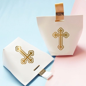 Elegant white paper candy boxes with golden cross patterns and ribbon handles for weddings