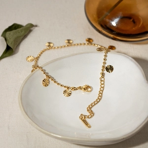 Detail of 18K gold stainless steel Cuban chain anklet with sunburst charms on ceramic