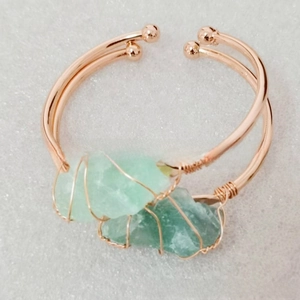 Detail of rose gold wire-wrapped open bangles featuring irregular green natural stones