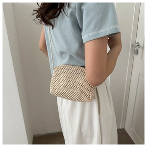 Detailed side view of a natural woven beige crossbody shell bag on a model