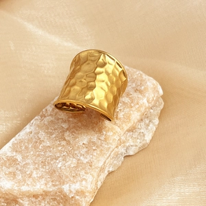Golden hammer-textured wide open ring made of stainless steel on natural stone base