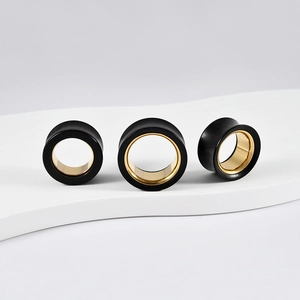 Three black and gold surgical steel ear gauges on white wave display in different sizes