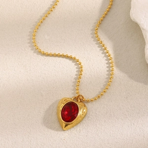 Close-up of a gold 18K plated stainless steel heart necklace with a red gemstone on bead chain