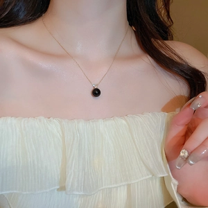 Detailed view of a black round pearl pendant with a small zircon on a golden fine chain
