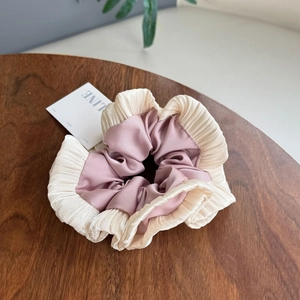 Detail of pink and beige satin scrunchie with pleated edges on a wooden table