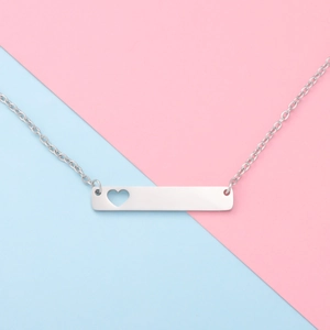 Macro shot of silver bar necklace pendant with hollow heart detail on split pastel background