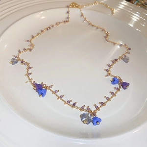 Macro detail of golden necklace with purple and blue flower beads on ceramic plate