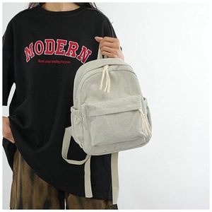 Close-up of light gray corduroy backpack with zipper detail and woven rope decoration