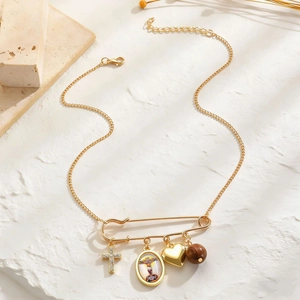Detail of gold safety pin necklace with cross, Maria medallion and heart pendant