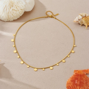 Minimalist gold snake chain necklace with round pendant discs on a beach shell background