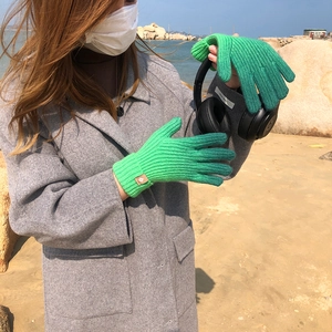 Close-up of green ribbed knit gloves worn by a woman at the beach with natural lighting