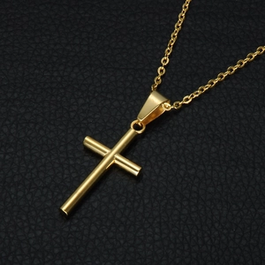 Close-up of a polished gold cross pendant necklace on a black textured leather surface