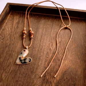 Detail of a resin heart pendant with marbled texture on a brown cord with accent beads