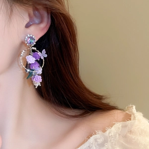 Gros plan d'élégantes boucles d'oreilles fleurs mauves avec papillon et longs pompons