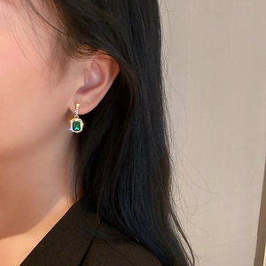 Macro view of green emerald-cut earrings with gold plating and clear crystal accents