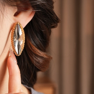 Detail view of oval crystal earrings with gold trim worn by a model in soft lighting