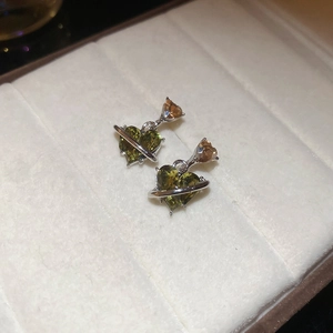 Detail of heart-shaped olive green and amber stud earrings on white velvet background