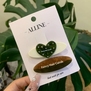 Détail de pinces à cheveux en acétate cœur vert et ovale marron avec des strass