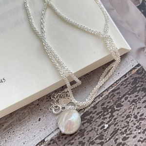 Detail of S925 sterling silver chain with a baroque pearl pendant on an open book