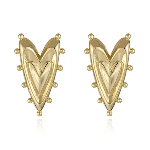 Detailed close-up of golden heart earrings with decorative ball-shaped rivets and mirror finish