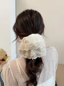 Detail of a large white double-layered lace hair scrunchie with delicate wavy embroidery