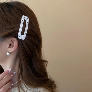 Close-up of white leather hair clip with black polka dot stitching worn by a model