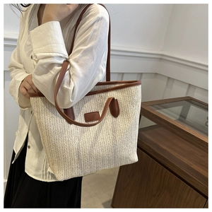 Detail of a beige woven tote bag with brown leather straps shown on a model
