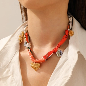 Detail of silk scarf necklace featuring golden heart, flower, and round coin charms