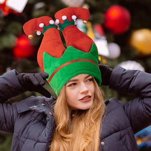 Funny red and green Christmas elf hat with bells and pompoms shown in festive setting